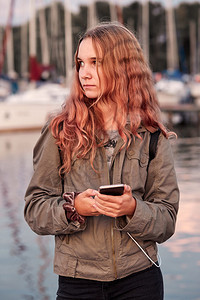人们年轻女使用手机智能站在湖边Candid人旁边的码头上真实时刻情况头发日落图片
