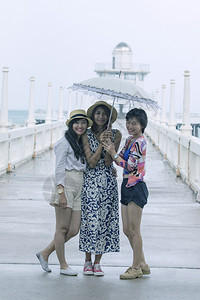 3名年轻的青亚洲女朋友在雨季一个伞下气候生活方式旅行女士图片