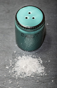 盐沙摇晃器和石黑桌上的研磨盐在陶瓷摇晃器周围切除白盐食物辛辣的桌子图片