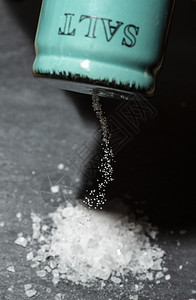 结石摇床盐沙晃器和石黑桌上的研磨盐在陶瓷摇晃器周围切除白盐厨房背景图片