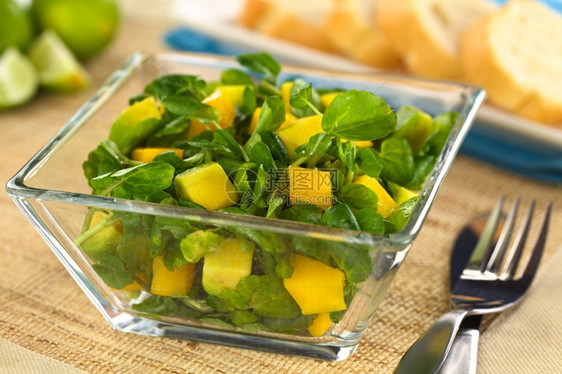 豆瓣菜玻璃碗中的新鲜水芒果和鳄梨沙拉后面有包选择焦点前面有芒果和鳄梨片刀具盘子图片