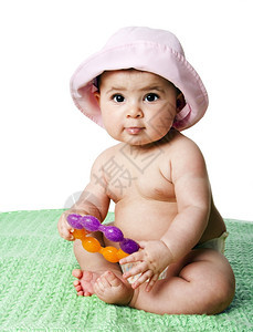 美丽的坐在绿毯子上着的漂亮可爱白人西班牙女婴拿着橙色和紫牙戒指玩具戴着粉色帽子与世隔绝紫色的女孩图片