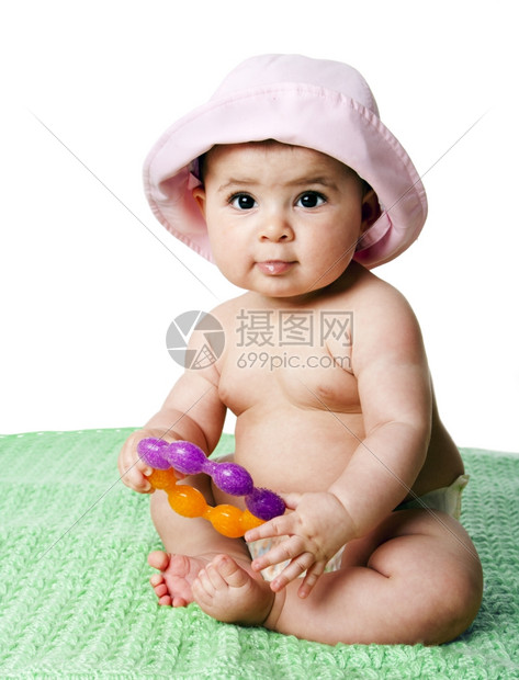 美丽的坐在绿毯子上着的漂亮可爱白人西班牙女婴拿着橙色和紫牙戒指玩具戴着粉色帽子与世隔绝紫色的女孩图片