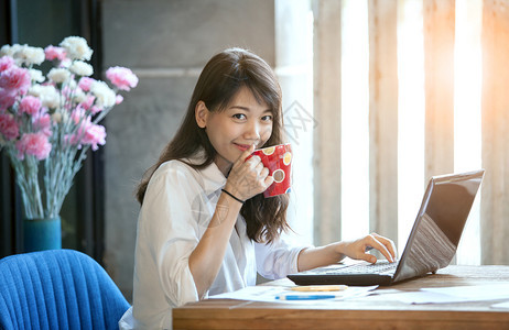 年轻亚洲女在自由职业者工作时喝着热咖啡的快乐笑脸电脑热的眼睛图片