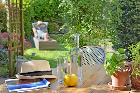 靠近水饮料和苹果在花园的木桌上女人坐在日光浴背景上靠近饮料和苹果在木桌上女人坐在日光浴背景上桌子与喝自然图片
