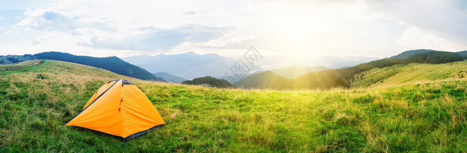 在草原上的橙色帐篷在明日阳光下有青草的山丘上云彩天空下有绿草夏季风光月景观全美橙色帐篷在草地上明亮的岩石营图片