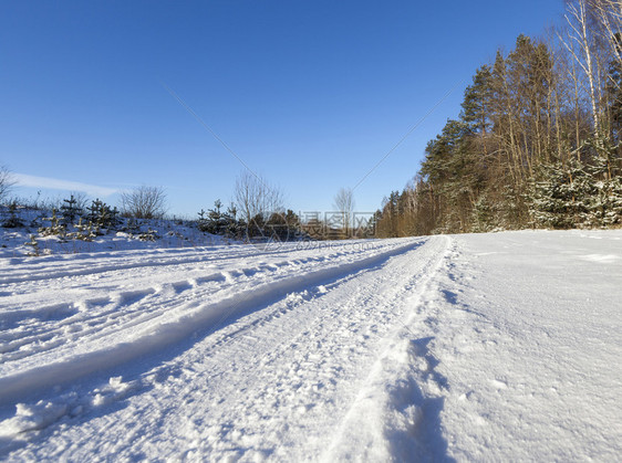 下雪的在地面上形成了汽车的痕迹和弯曲一张贴近照片上面有树木和蓝色天空一条冬季沥青路另一条是冬柏油路农村天图片