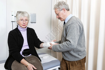 医生在院急救室检查一名老年妇女的绷带扭伤手腕并进行体检伤害房间听诊器图片