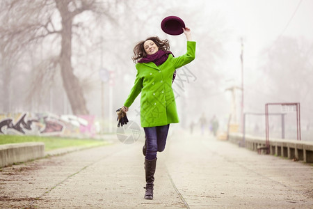快乐的年轻女子在福吉日带着帽子在脚路跳跃绿微笑跑步图片