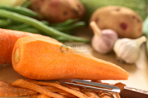 果实胡萝卜加剥皮机和其他蔬菜绿豆土木板上大蒜选择焦点聚胡萝卜皮的左边缘木制削皮机剩下图片