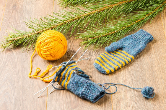 柔软的黄色温暖线针手套和木本底松树枝的柱形图片