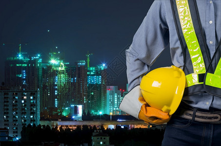 亚洲工程师手持黄色头盔在公寓楼新建筑和起重机的背景下保护工人安全手持黄色头盔的亚洲工程师男人项目商图片