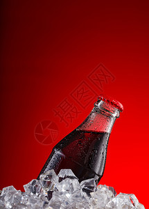 湿瓶中的棕色碳酸饮料红背景中的冰块带有红色帽湿瓶中的棕色碳酸饮料红背景中的冰块带有红色帽棕的苏打瓶子图片