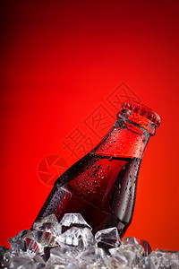 白色的新鲜红背景冰块上误装了一瓶深碳酸饮料和红帽在冰块上误装了一瓶深碳盐饮料和红帽子棕色的图片
