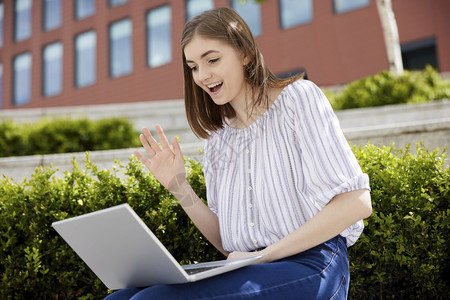 年轻女性手持笔记本电脑在大学校园里视频聊天图片