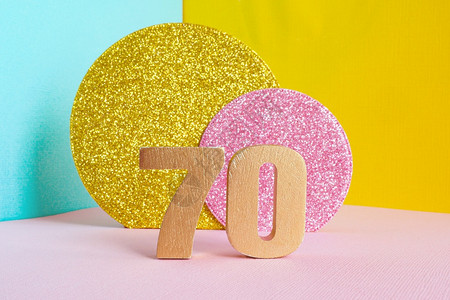 黄色夹心蓝数字金牌70号子在多色蓝黄粉红背景和两颗闪亮的金子和粉红色圆圈生日快乐贺卡概念片几何学祝贺背景