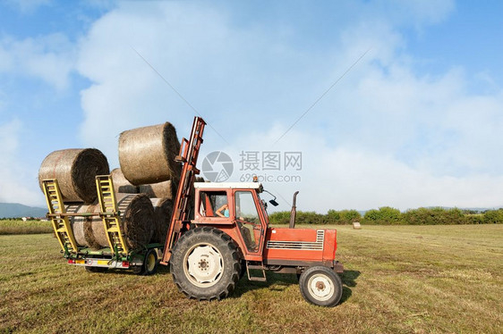 包云拖拉机在野外收集干草篮子和装上农车天空图片