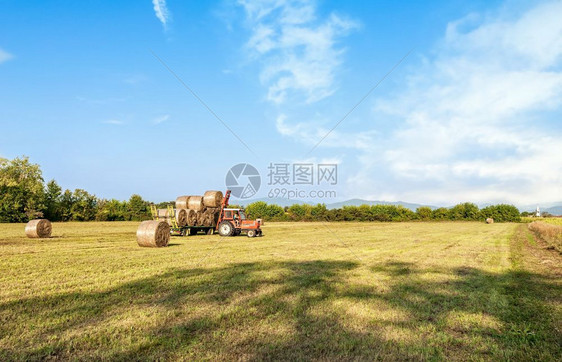 季节云收成拖拉机在野外收集干草篮子和装上农车图片