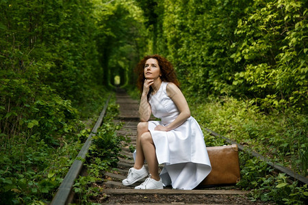 女在森林隧道铁路轨迹上的旧式手提箱坐着身服装的妇女旅程概念女士运输图片