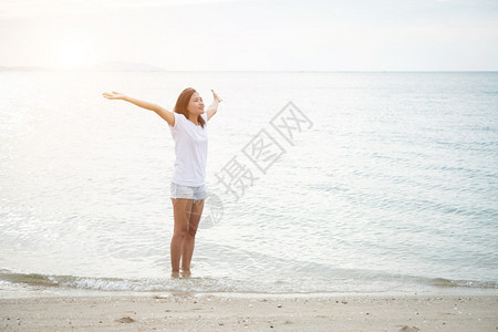 年轻美女站在海滩上赤脚放轻松的节日中举起双臂在空中伸展女夏天快乐的图片