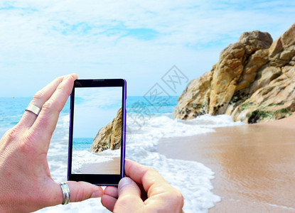 用手机拍摄海滩的手部特写背景图片