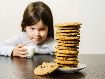 曲奇饼照片中一位年轻女孩在拿着一杯牛奶时盯着一堆巧克力薯片饼干看专注于上尽管童年图片