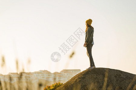 日落在悬崖上挂着黄色帽子的女人看到海滩秋天女图片