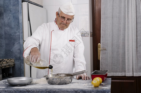 面包师在一家厨房的里把油放进钢碗里用具搅拌机炊图片