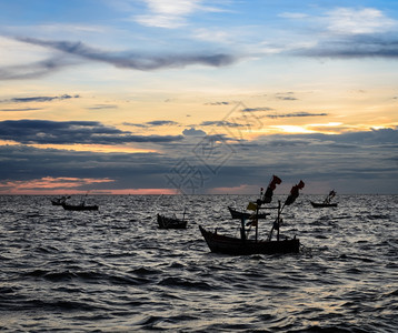 泰国在日落海景阳光灿烂的太花天空下海上渔船的休光月水丰富多彩的海滩图片