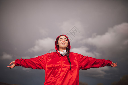 下雨年轻女子在天与衣和耳机一起站在田地上放松红色的图片