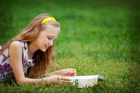 说谎童年可爱的9岁女孩躺在绿色草地前线阅读一本书学习图片