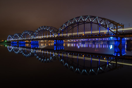 水晚上在里加的铁路大桥上在道格瓦河有美丽的反光火车在桥上移动长期照射蓝色的运动图片