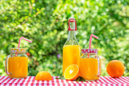 绿色天然背景生态友好型玻璃软件瓶和橙汁罐头以及橘花边桌布上橙子加的罐装餐桌布上橙子户外玻璃器皿饮料图片