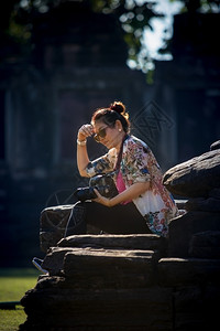 目的地数码单反活动带着Dslr相机的女游客手握着照相机用美丽的阳光坐在岩石上图片