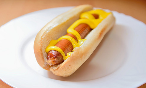 卷美国人不良一个煮熟的热狗在一个简单的软面包里和芥末加在白色盘子上图片