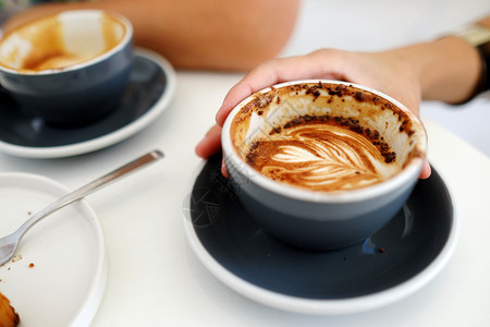 马克杯喝在咖啡馆背景顶端观点食物和饮料概念的白桌上握着咖啡杯的手浓图片