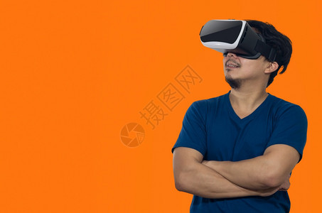 面具未来派耳机有虚拟现实头盔的年轻人站在橙色背景的室内青年拿着虚拟现实头盔的年轻人图片