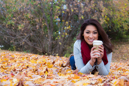 趴在秋季落叶上喝咖啡的女性图片