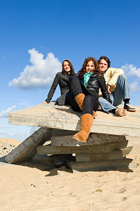 三个年轻的成人坐在沙滩上的水泥板在美丽的秋天下午城市男人微笑图片