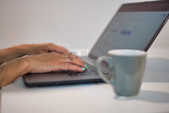 妇女手拿着贝壳触摸现代笔记本电脑边喝咖啡上还有技术和商业概念打字工作在职的图片