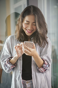 以快乐的情绪寻找和智能电话上的信息聊天而欢笑的亚洲年轻女手机讲话移动电图片