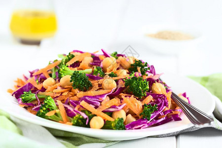 新鲜红菜卷小鸡豆胡萝卜和花椰菜沙拉盘子上以自然光显示有选择的重点焦在红色卷心菜奇克比亚胡萝卜和布罗科利沙拉的图像中间新鲜的生脉冲图片