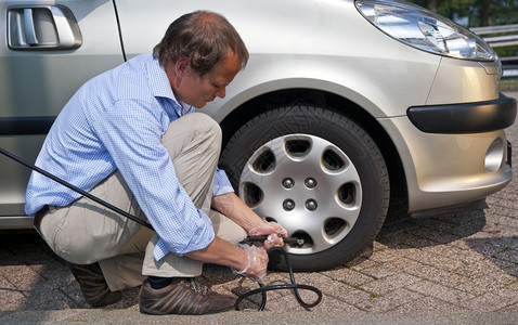 车辆帽旅行跪着的男人在加油站他的车右前轮胎充气图片