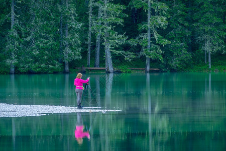 自然奥地利一种女摄影师站在水的边缘森林湖上与一名三脚女摄影师拍照片在Forest湖上女孩摄影师站在水边用一个三脚女摄影师拍照图片