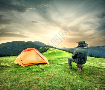 旅行户外门14坐在帐篷旁的人看着山上日落的太阳男人看着帐篷旁边的人看着日落太阳图片