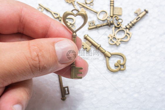 天浪漫的白色手握着一个心脏形状的钥匙在白色背景上的底键而在其他密钥之上图片