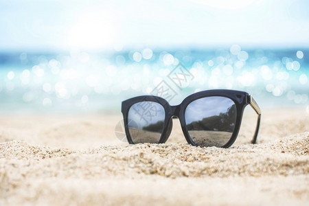 水可选择的墨镜放在沙子上自然反射在两极透镜中背景的海模糊支撑图片