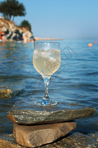 太阳海浪冲刷的岩石边杯白葡萄酒被海浪冲洗过休息滩图片