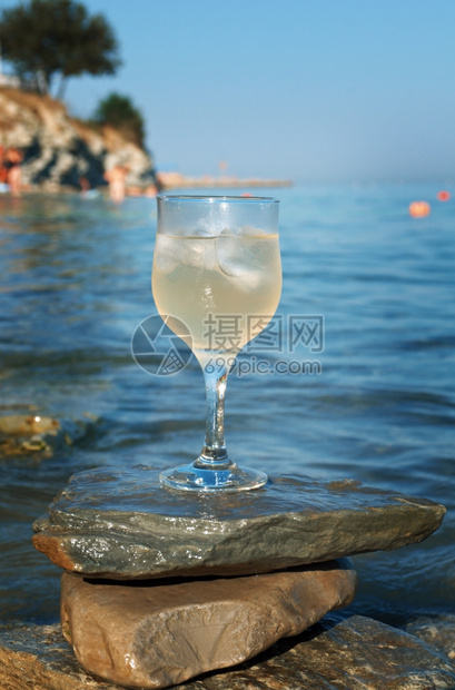 太阳海浪冲刷的岩石边杯白葡萄酒被海浪冲洗过休息滩图片