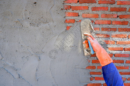 泥水匠石板人用橡胶手套木铁筋到砖墙背景的石膏水泥上用橡胶手套将蓝色长袖和橡胶手套拉在一起与复制空间闭合袖子红色的图片